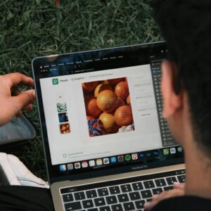 A man edits a fruit image on a MacBook Pro while sitting outdoors on grass.