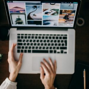Hands using a laptop to browse photo galleries, illustrating digital creativity and remote work.